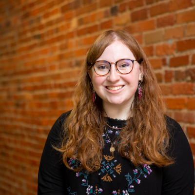 Photo headshot of smiling Emily standing in front of a brick wall