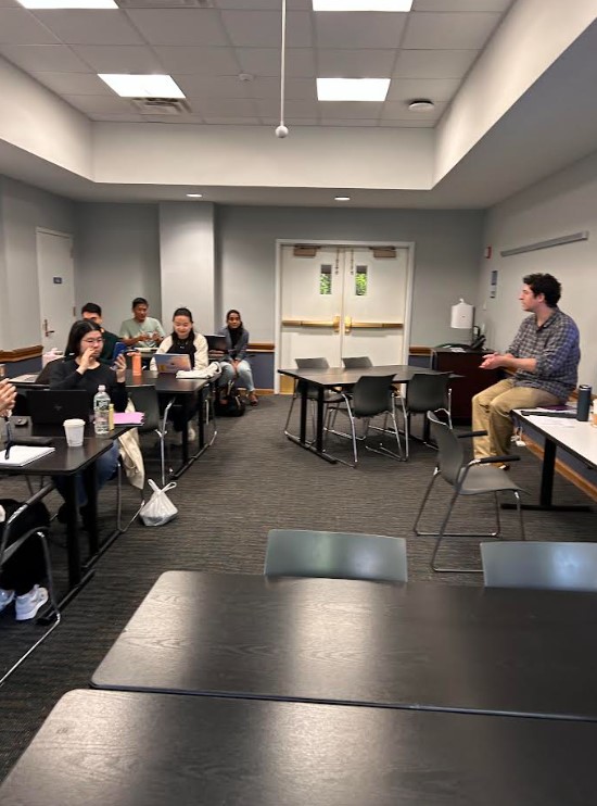 Graduate writing fellow gives lectures on writing organization to students. Students sit at tables listening to the lecture.