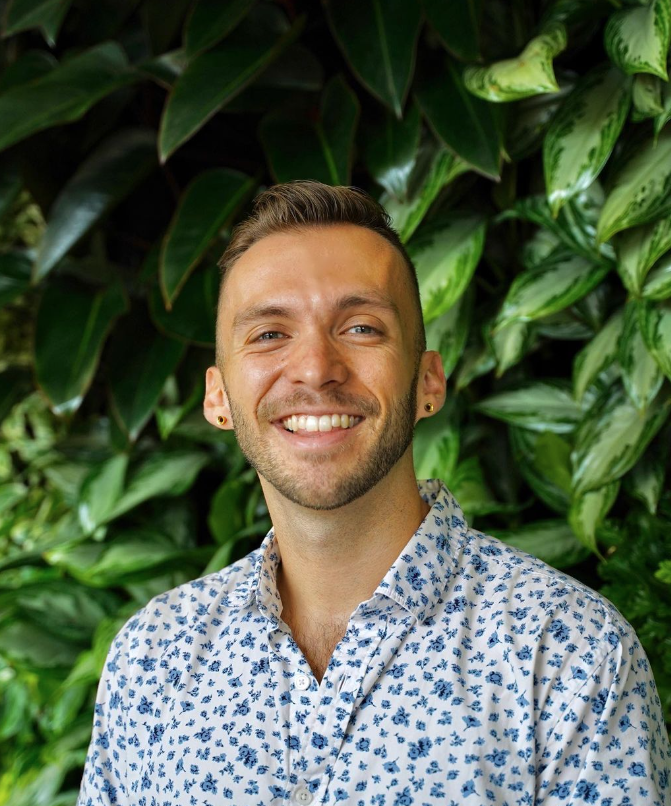 Caucasian male smiling with short brown hair and a white with blue printed shirt.