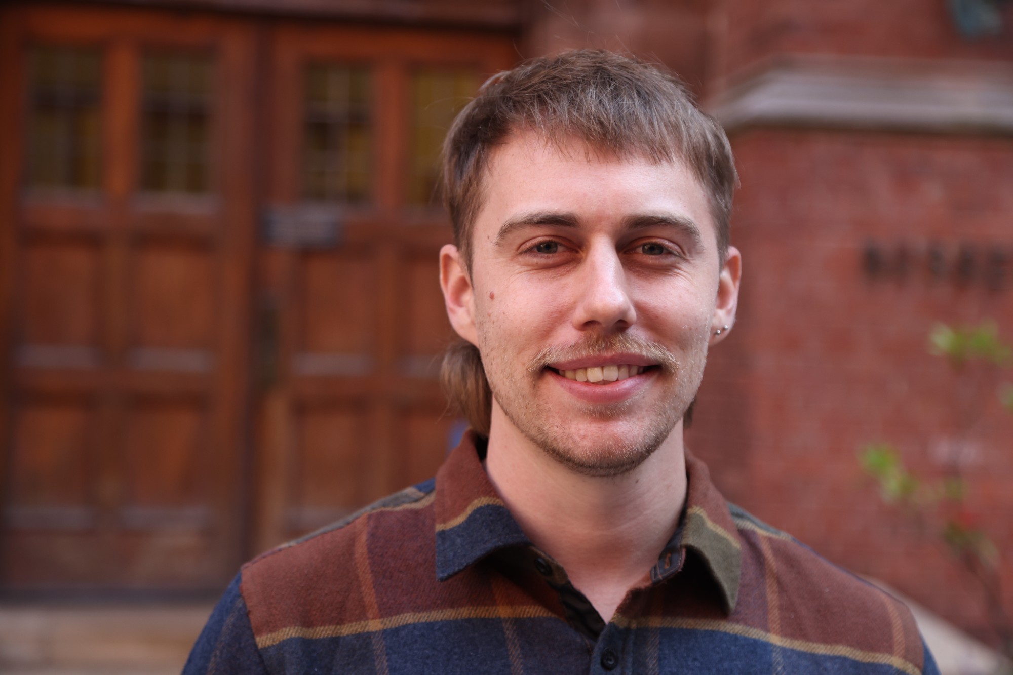 Headshot photo of someone smiling, set against the outside brick wall.