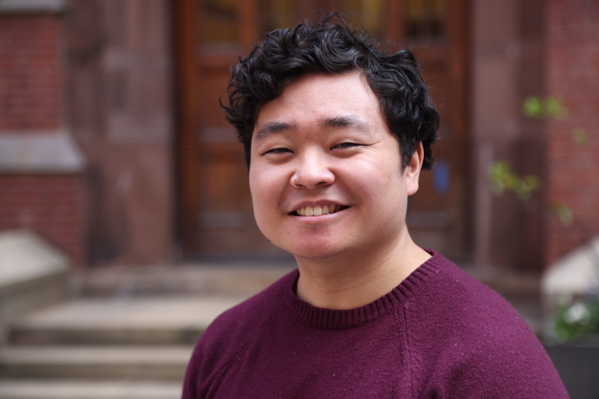 Headshot photo of someone smiling, set against the outside brick wall.