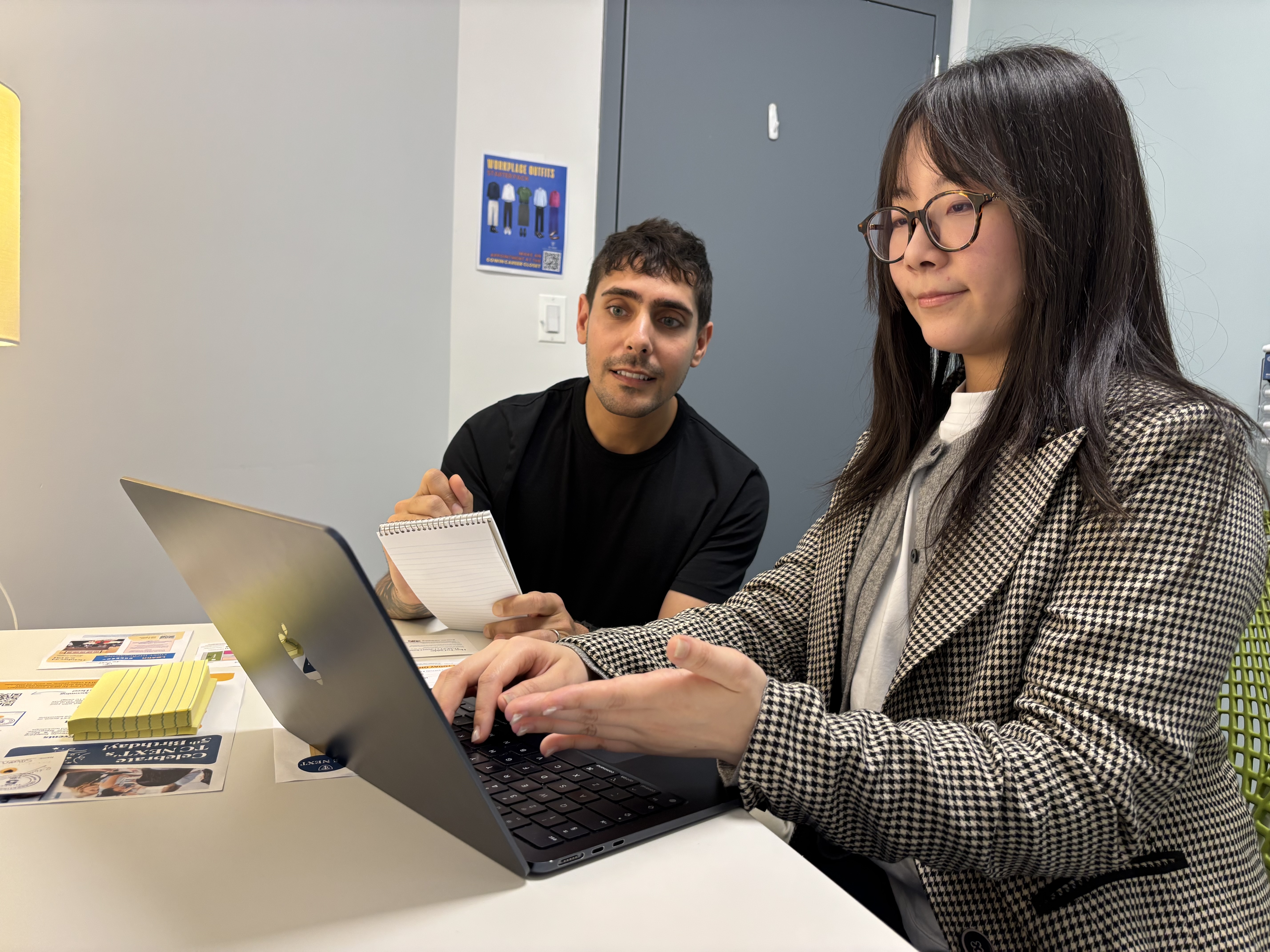Student sitting with mentor at table reviewing laptop content
