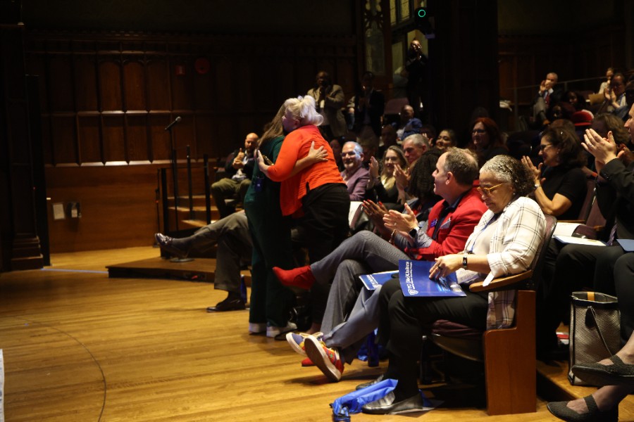 View of the audience seated in Milbank Chapel with two participants greeting each other and hugging