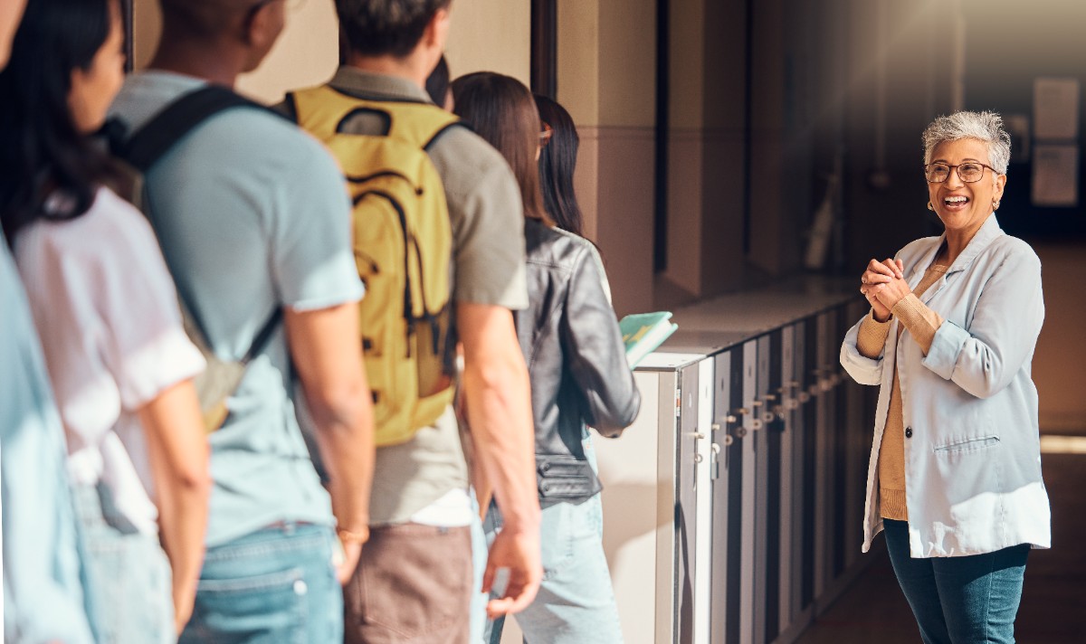 A woman smiling in a school hallway looking at a line of six students