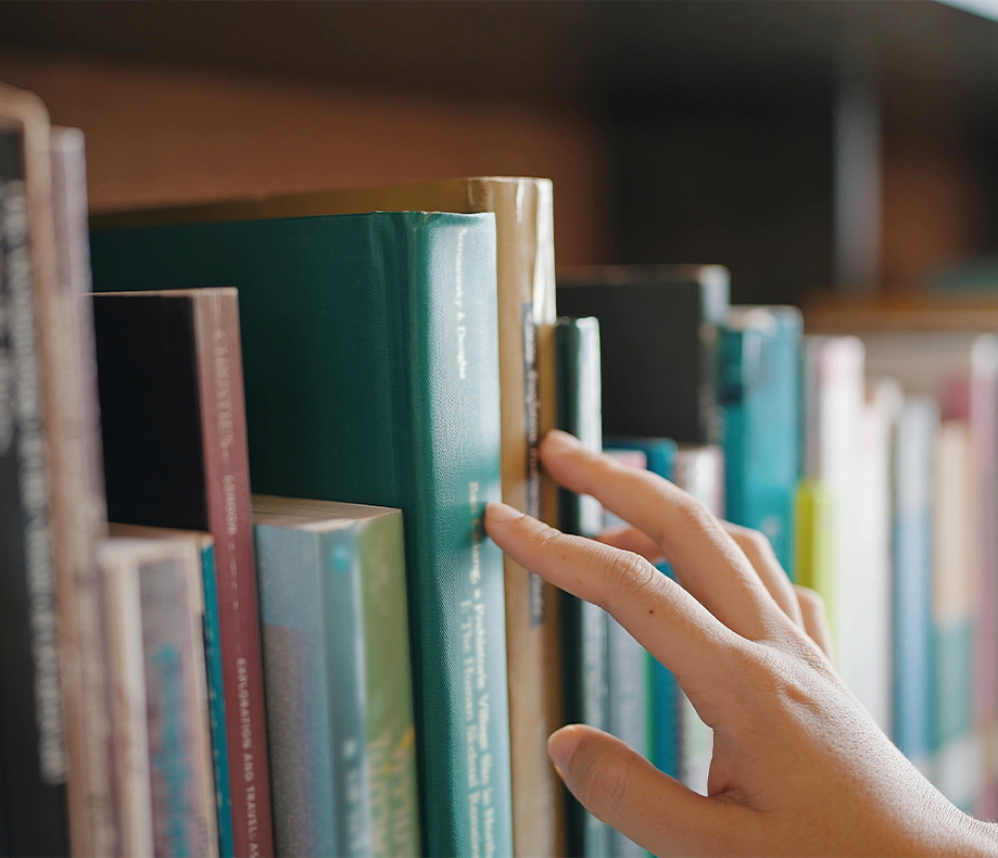 A close up shot of a hand touching books on a bookshelf