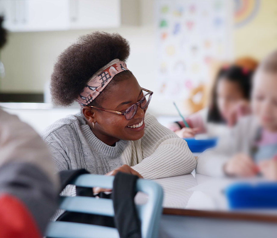 Smiling teaching leaning on students desk looking at their work