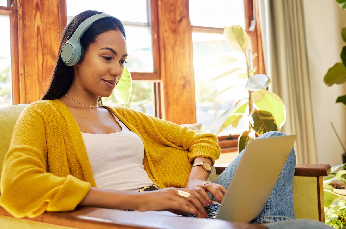 A woman wearing headphones sitting comfortably in a chair while typing on a laptop in her lap