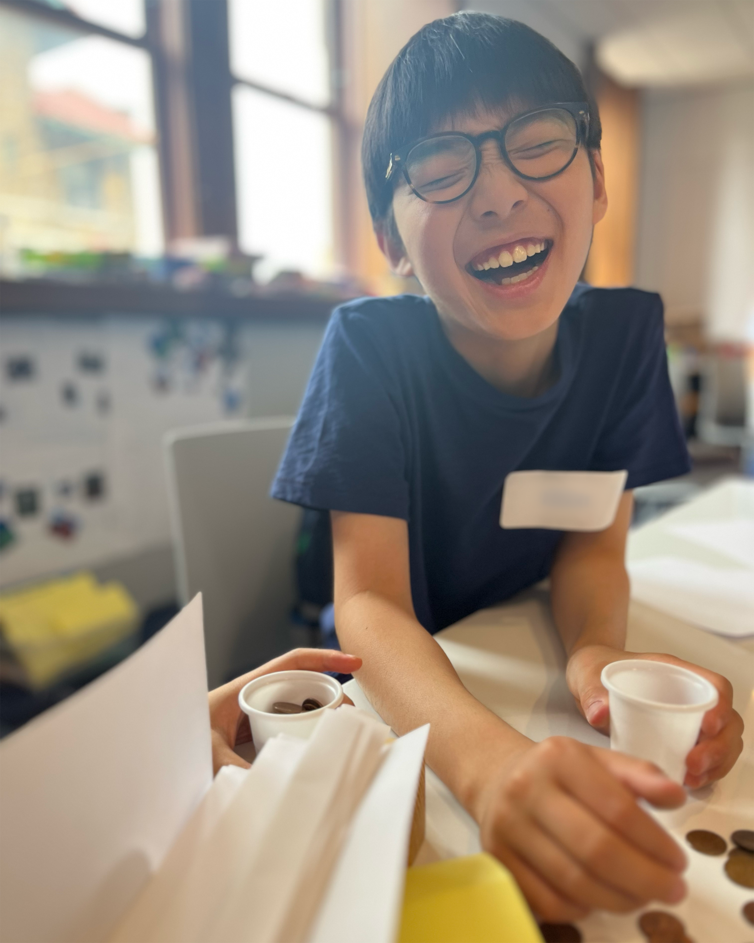 A child is laughing as his paper bridge design falls, spilling pennies onto the table.
