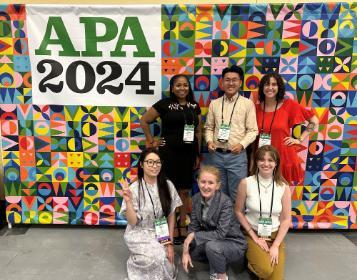 Group of six people posing in front of a backdrop sign for APA 2024