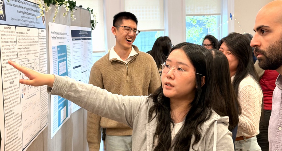 Students in the Psychology in Education program gathered next to their integrative project boards, pointing to documents on the board.