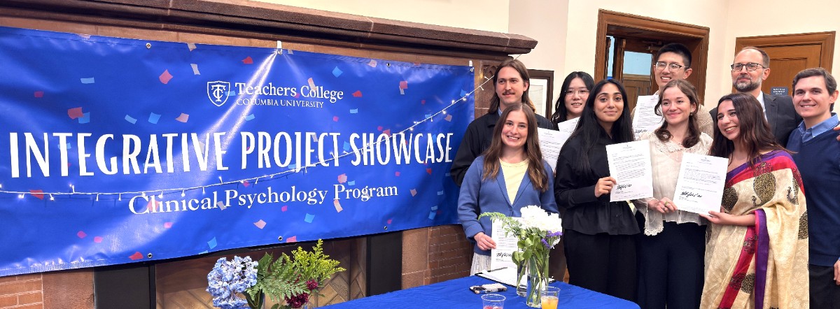 Students in the Psychology in Education program smiling and holding certificates next to a banner Integrative Project Showcase Clinical Psychology Program