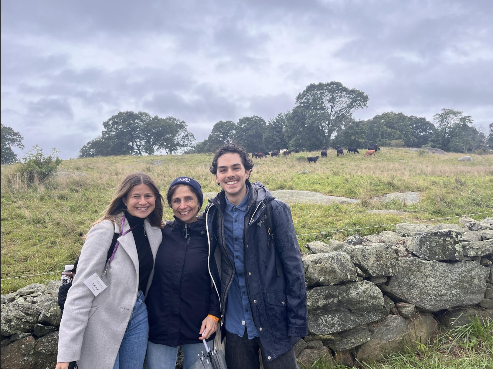 Two women & one man standing in front of pasture with cows