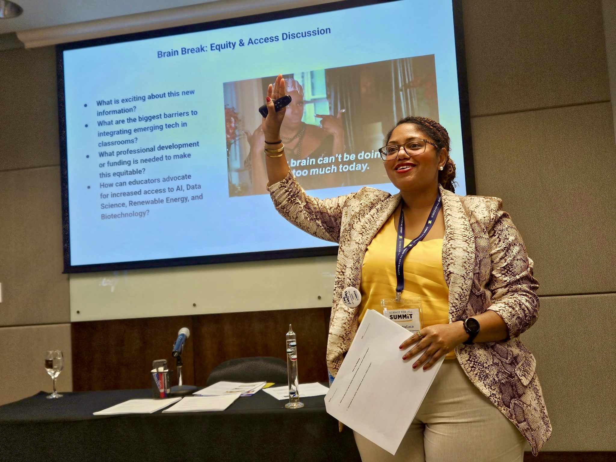 Chéla Wallace stands in front of a powerpoint presentation with her hand raised, facilitating a workshop.