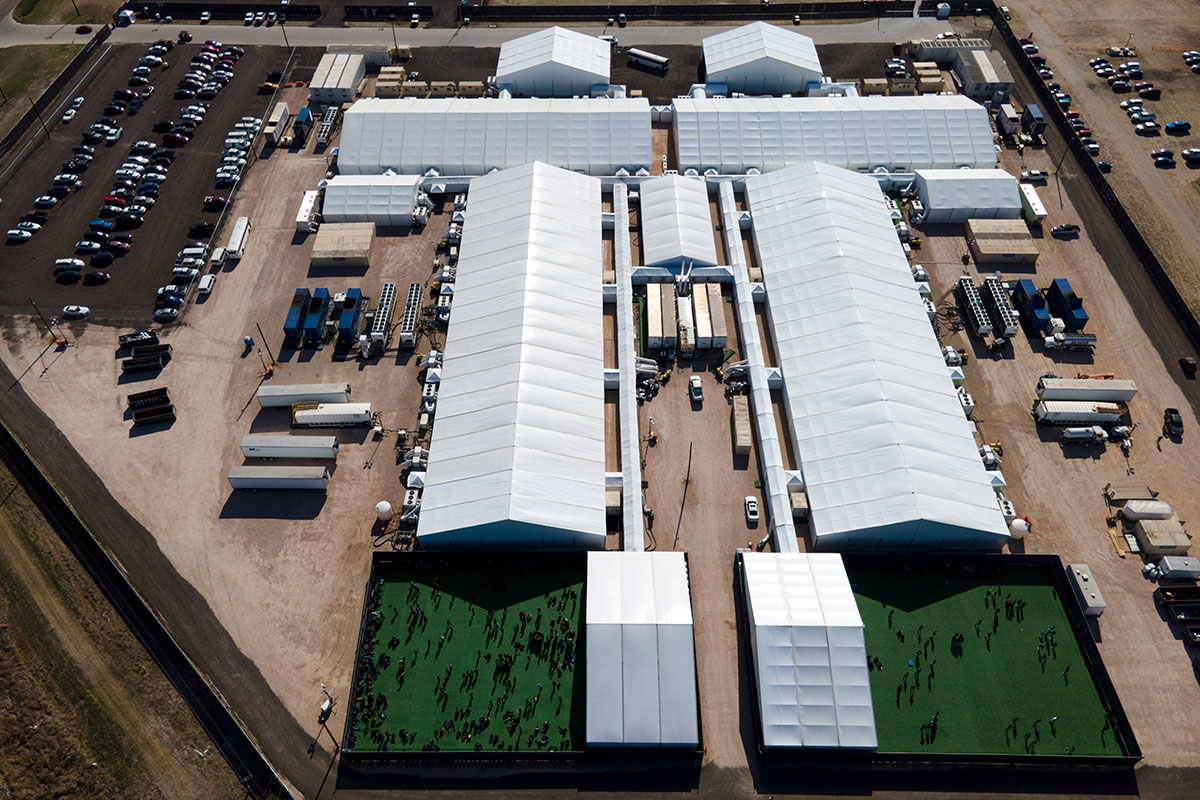 Migrants are seen in a green area outside of a soft-sided detention center after they were taken into custody while trying to sneak into the U.S., Friday, March 19, 2021, in Donna, Texas. A surge of migrants on the Southwest border has the Biden administration on the defensive. The head of Homeland Security acknowledged the severity of the problem Tuesday but insisted it's under control. (AP Photo