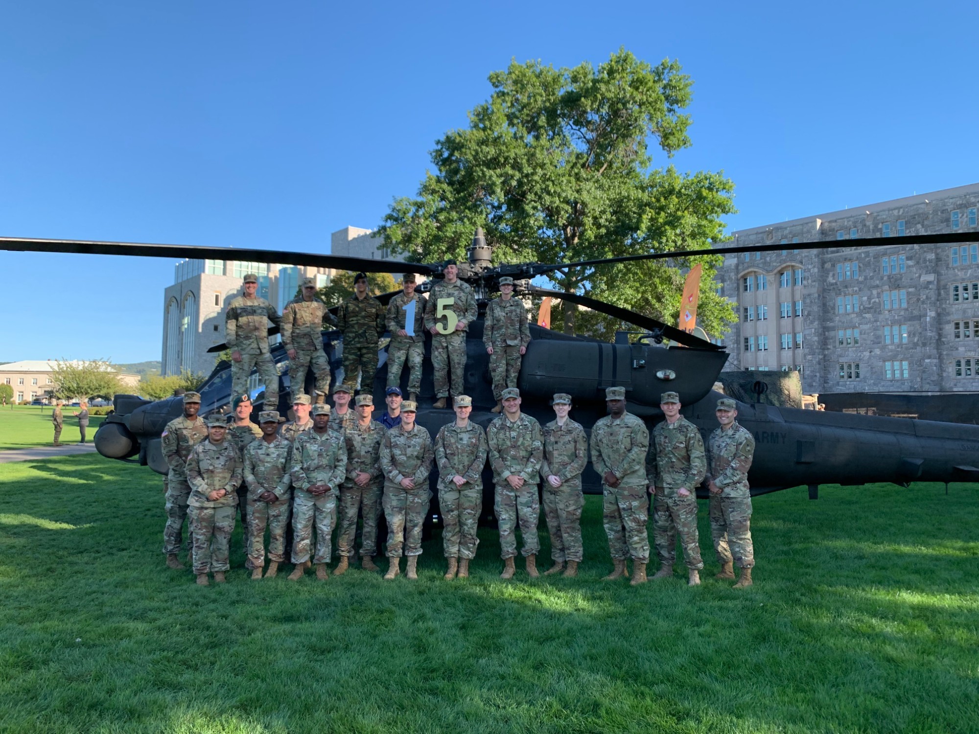 ELDP cohort 15 outside in front of helicopter wearing camos on a clear blue day.  Two members are holding large 1 and 5.