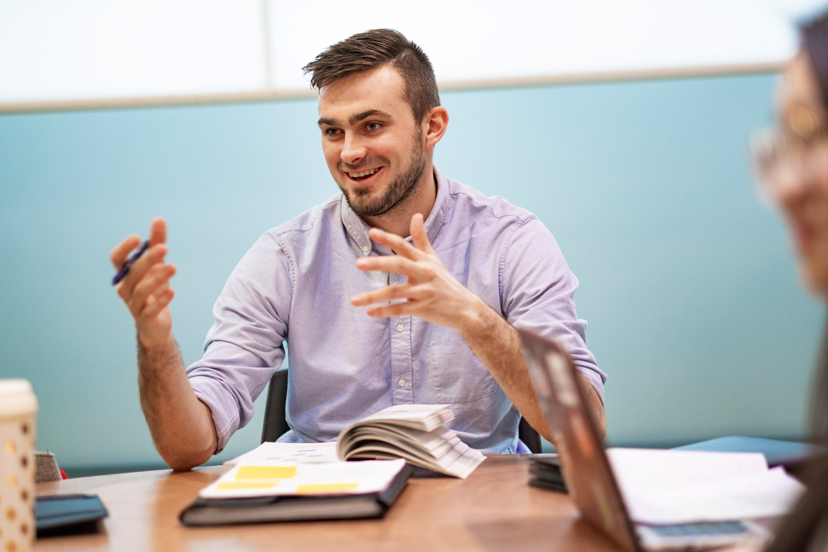 A graduate student has an animated conversation with his peers at TC.