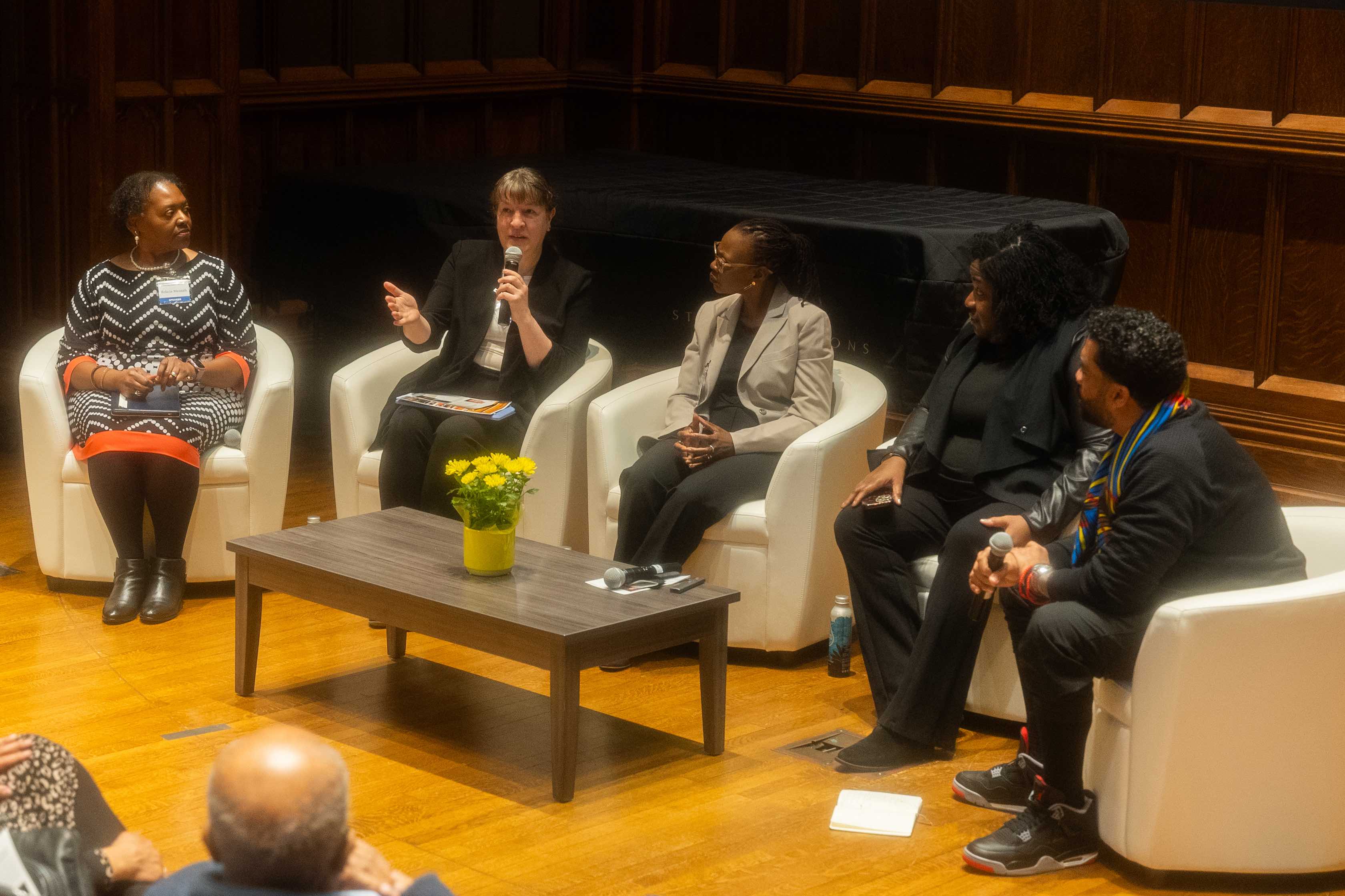 Five people deep in discussion, sitting on white chairs