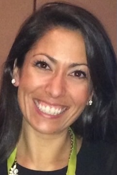 Michelle Troche smiling big at the camera. She has dark brown hair, fair skin and is wearing sparkly stud earrings