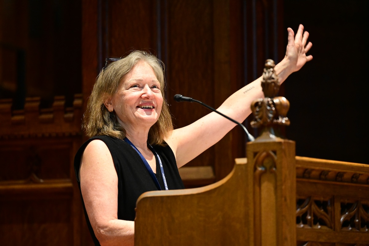 Celia Oyler standing at a podium, smiling with her arm raised