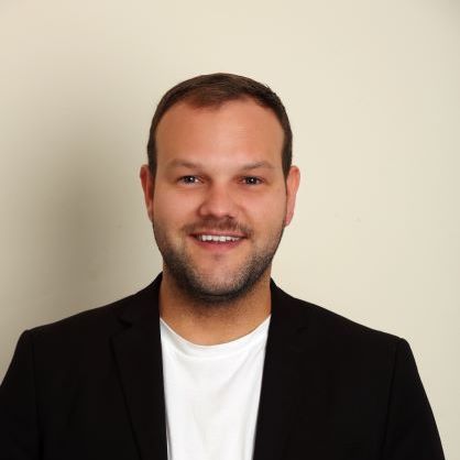 Cam Arnzen smiles at the camera, wearing a blazer and a t-shirt