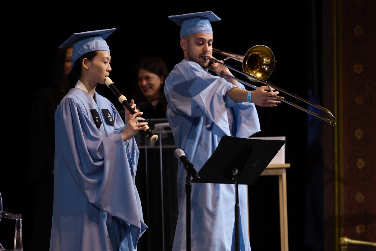 one graduate plays the obo and one plays the tuba, on stage at Convocation 2024