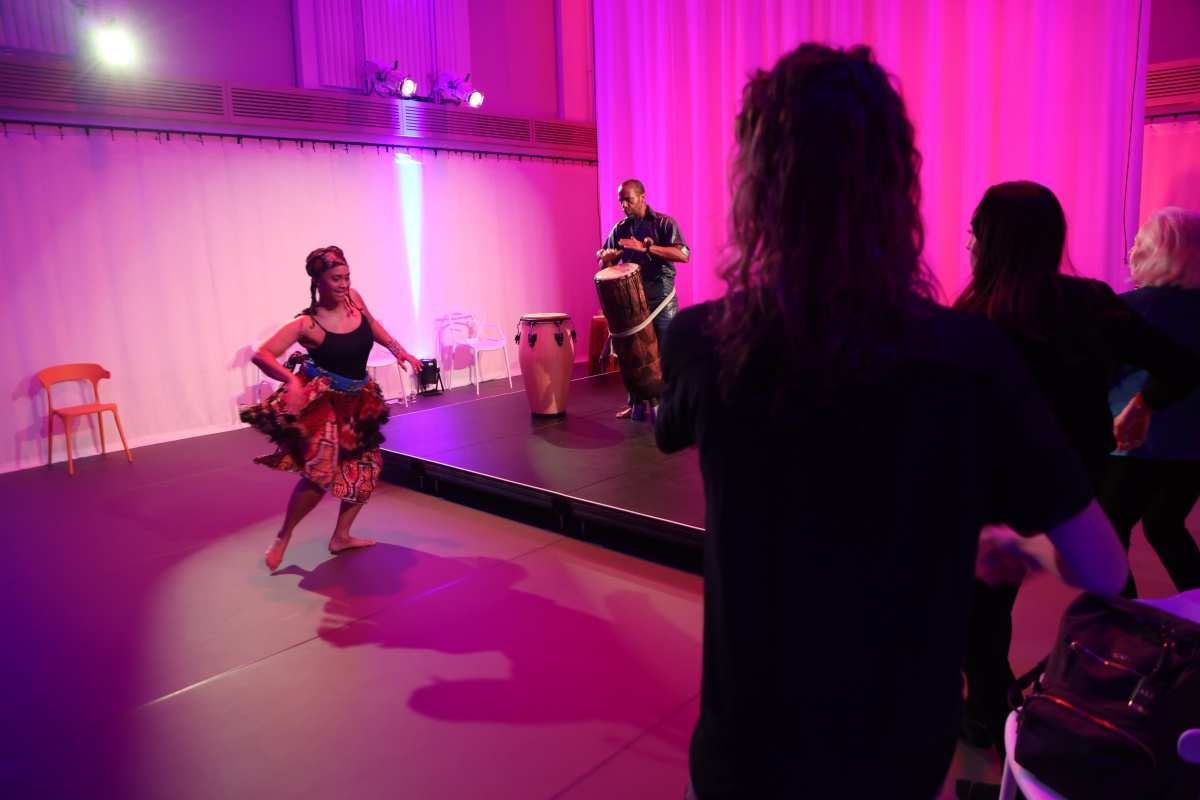 Dancer performs in a vast, pink-lit studio in front of an audience