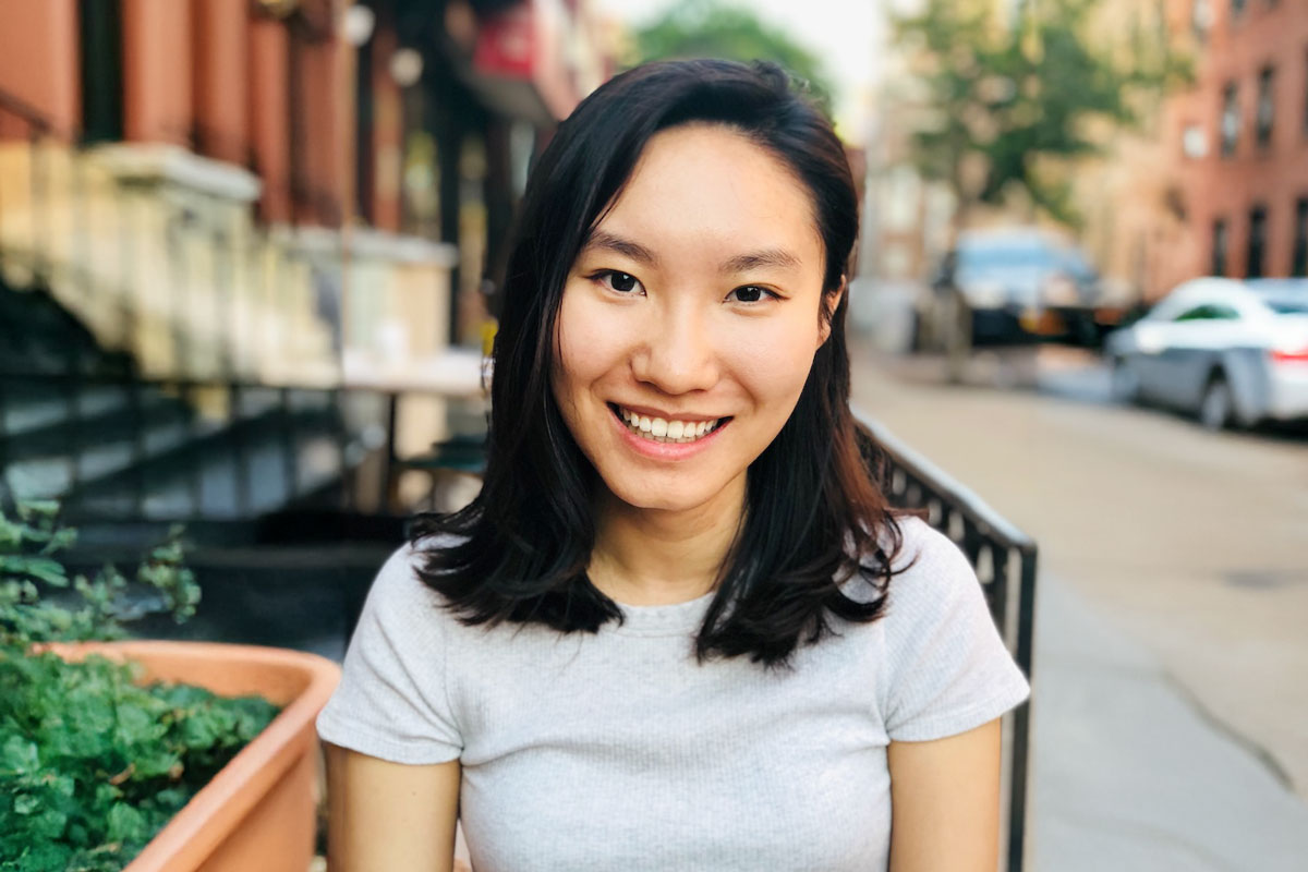 Yipu zheng smiles at the camera. She has collarbone-length hair and is wearing a white shirt