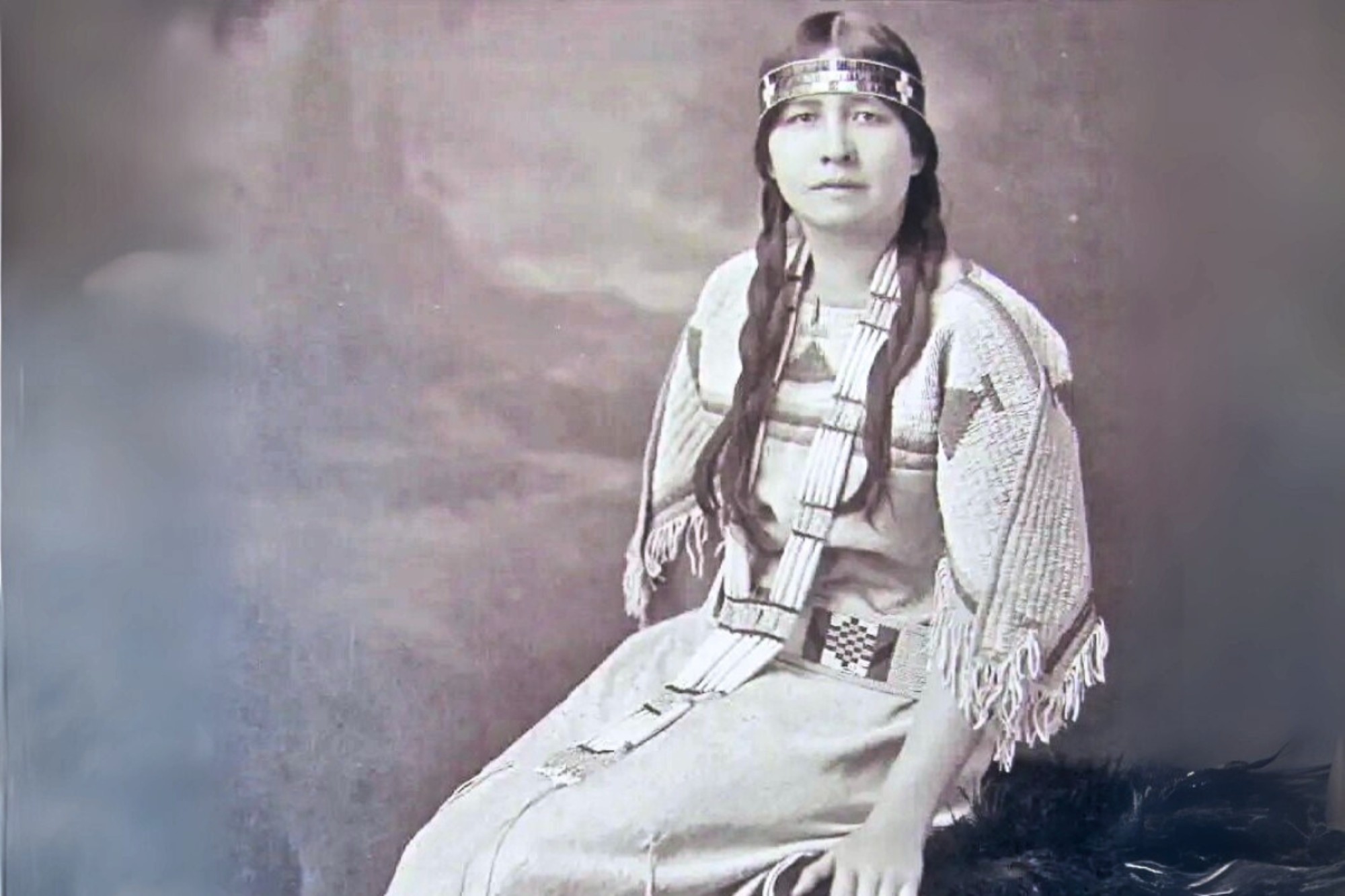 A balck and white photo of Ella Cara Deloria in traditional Sioux garments sitting on pelts