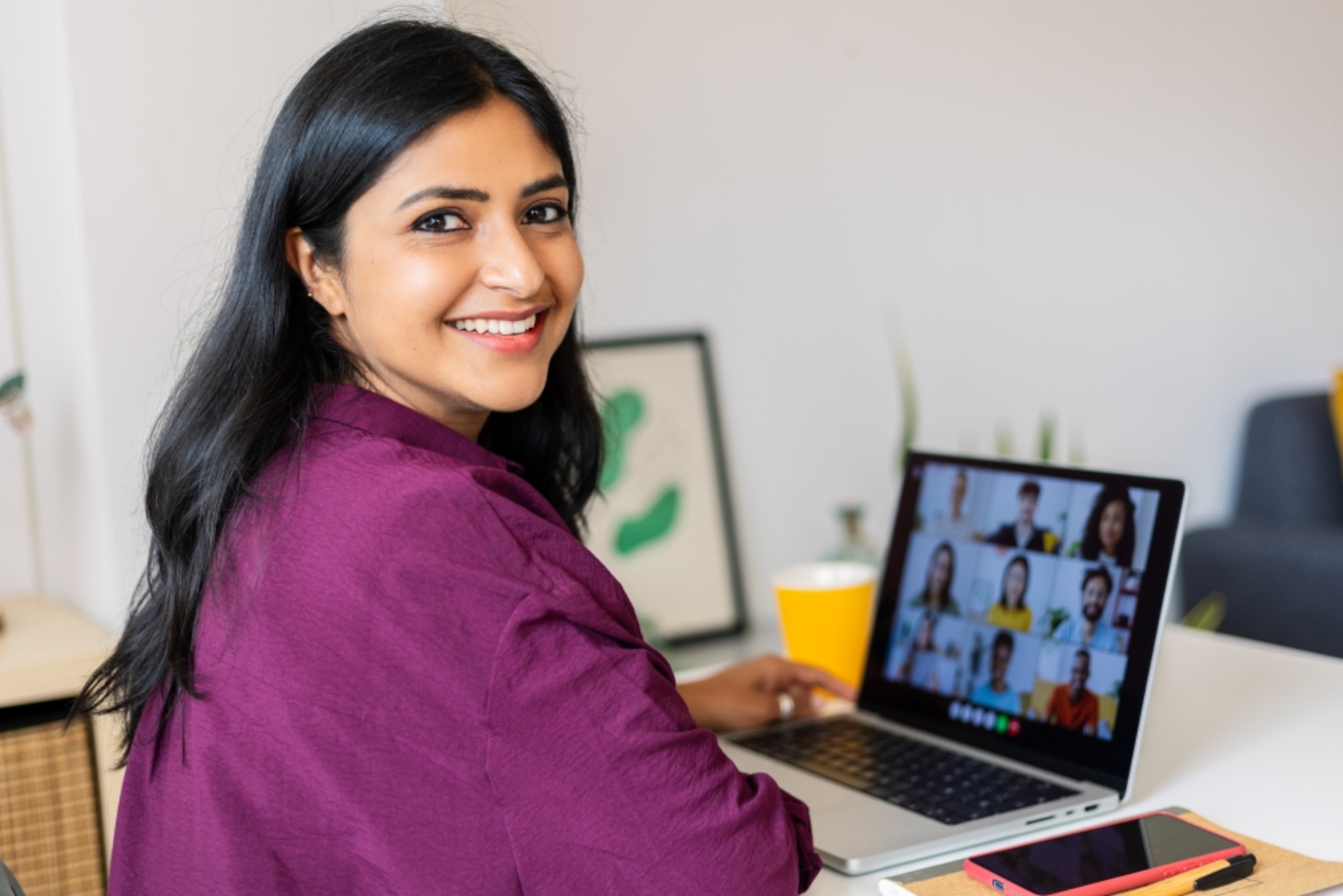 A woman smiling at the camera while on a video conference call on the laptop in the background